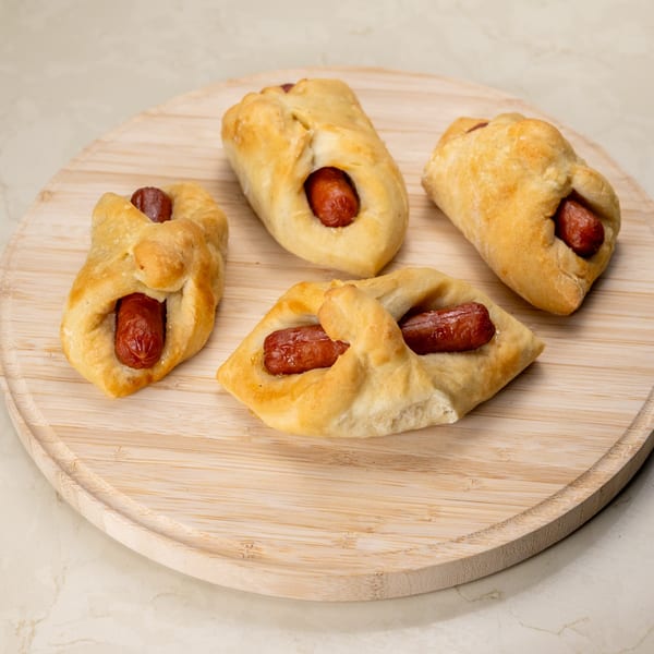 Four golden-brown Manske rolls, each with a hot dog peeking out, on a wooden cutting board.