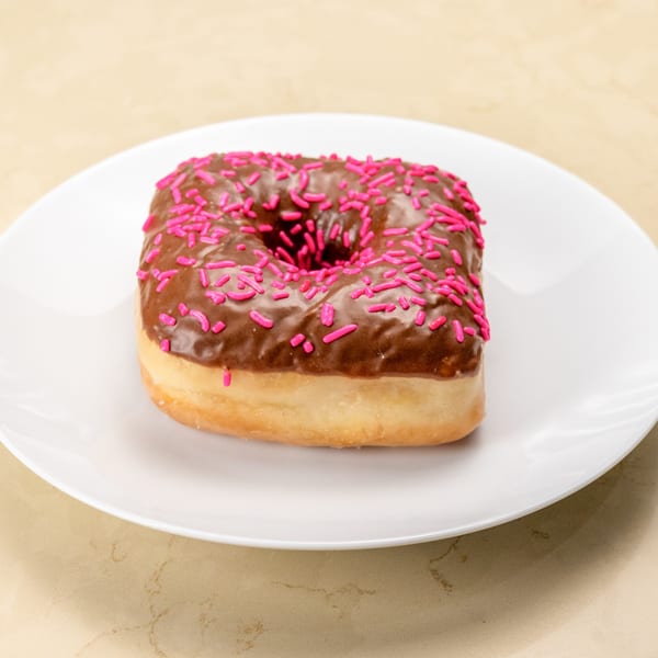 Square chocolate donut with pink sprinkles on a white plate from Gil's Broiler & Manske Roll Bakery.