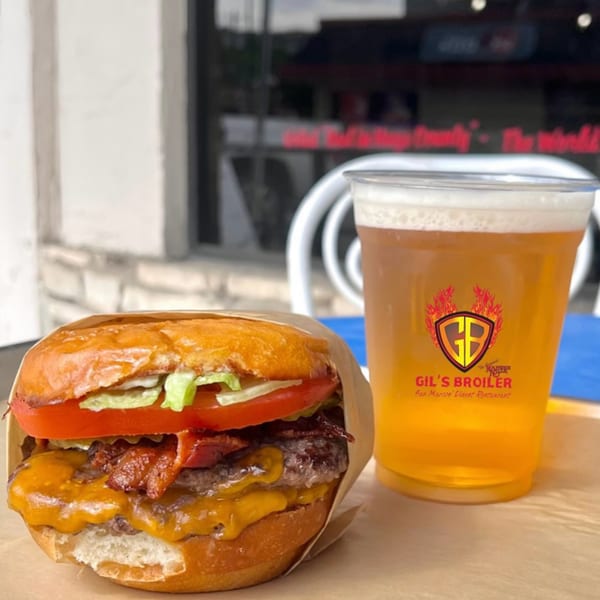A Gil's Broiler double cheeseburger with bacon, lettuce, and tomato next to a beer.
