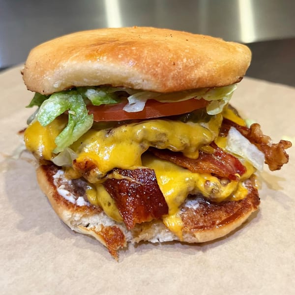 A double bacon cheeseburger from Gil's Broiler, with melted cheese, lettuce, tomato, and pickles.