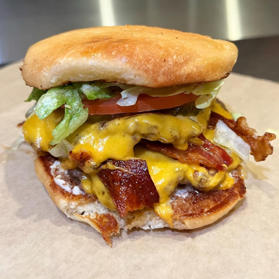 A double bacon cheeseburger from Gil's Broiler, with melted cheese, lettuce, tomato, and pickles.